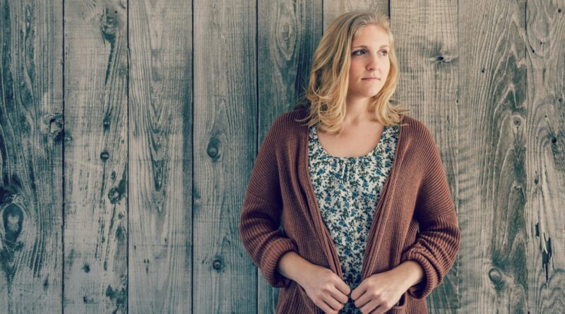 woman wearing brown cardigan leaning on wooden wall